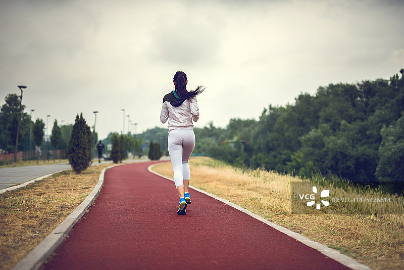 一个女人在运动跑道上跑步的后视图。图片素材