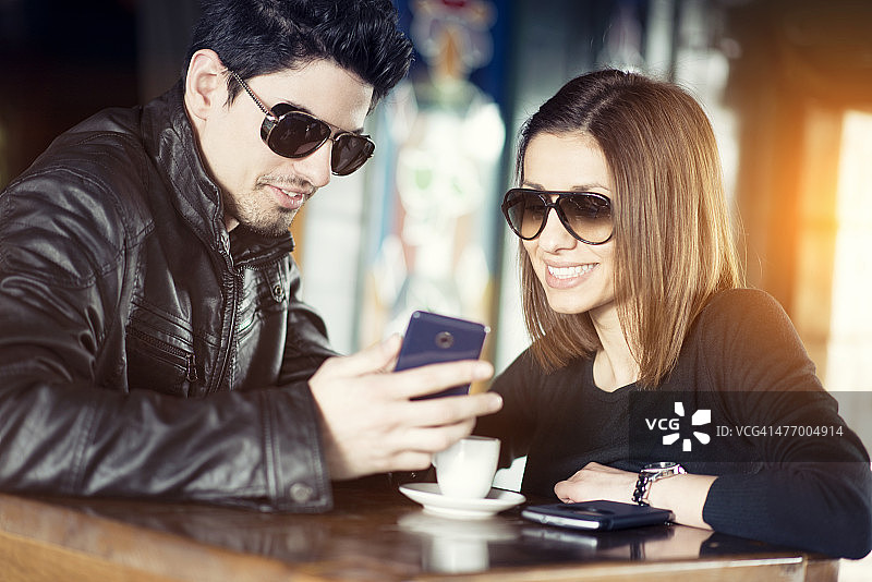 一对情侣在咖啡馆里用手机微笑图片素材