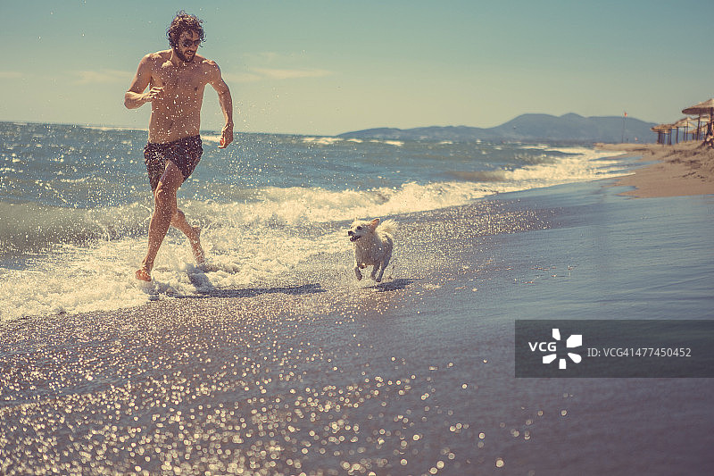 一个人和他的狗在沙滩上跑步图片素材