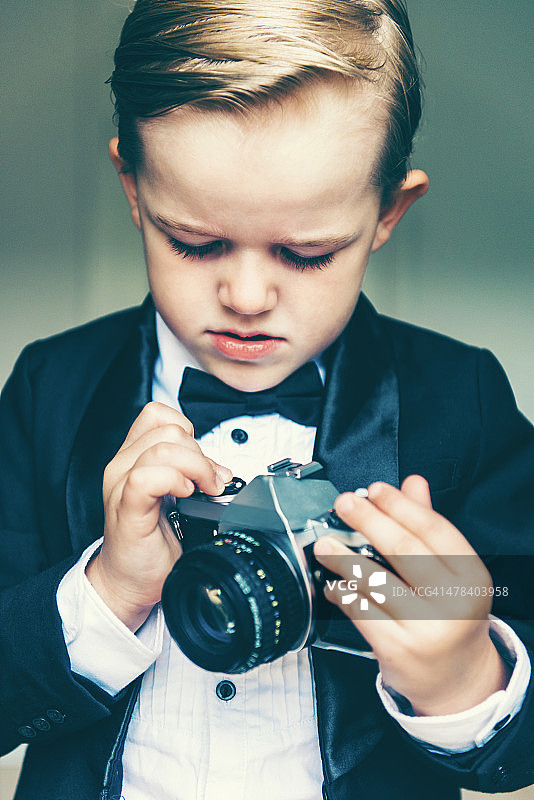 男孩穿着燕尾服，玩着复古相机图片素材