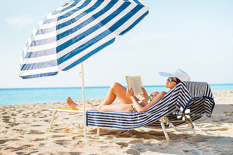 穿着比基尼的漂亮女人在海滩上看书和晒日光浴图片素材