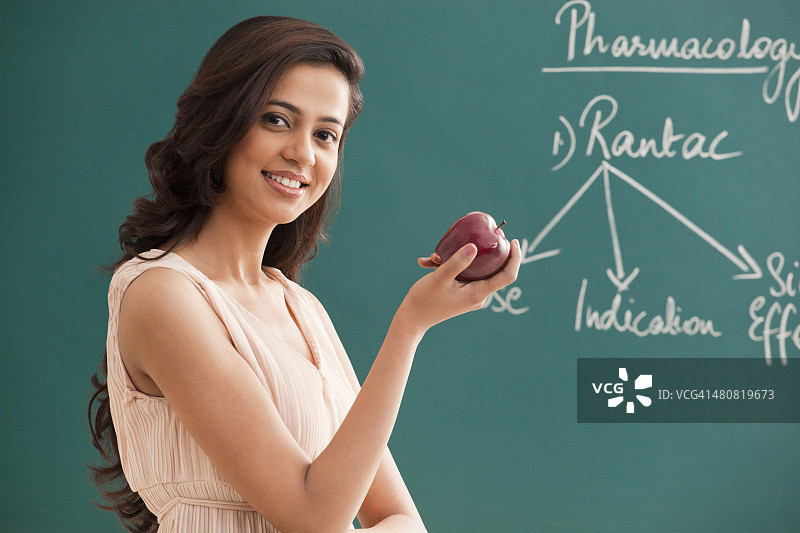 一名年轻女教师在黑板上举着苹果的肖像图片素材