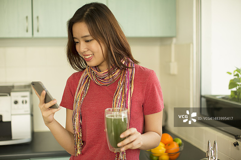 年轻的亚洲女人在厨房看她的手机图片素材
