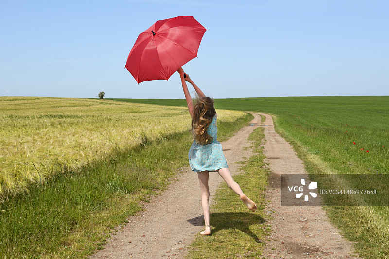 少女撑着红色阳伞站在土路上图片素材