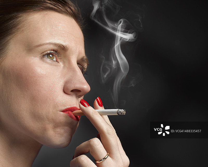 一名40岁女性在黑色背景下吸烟图片素材