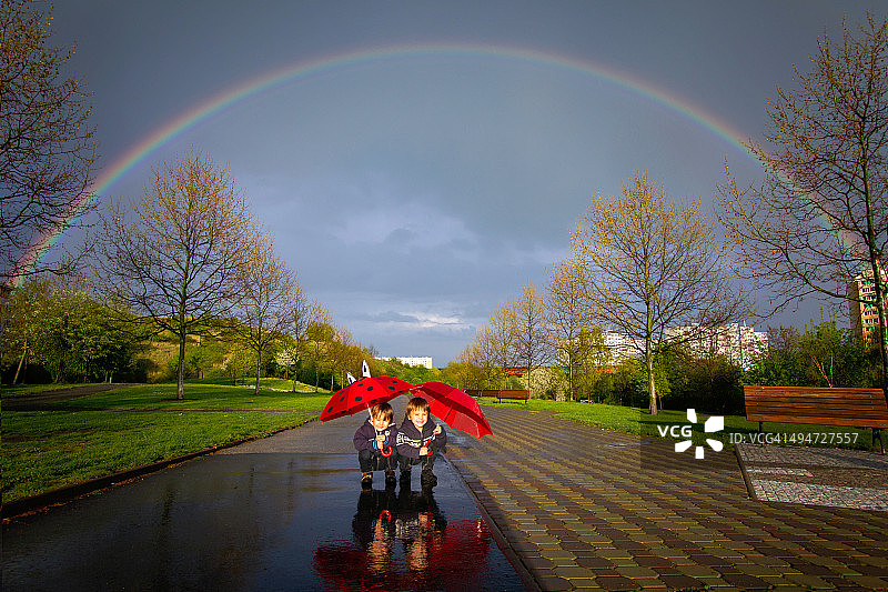 两个男孩在美丽的彩虹下打着伞图片素材