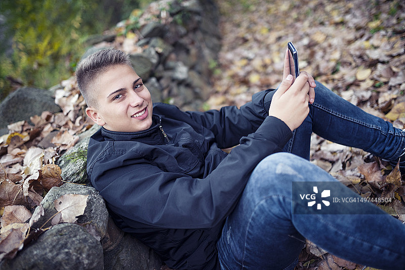 微笑的少年如何在公园里使用他的智能手机图片素材