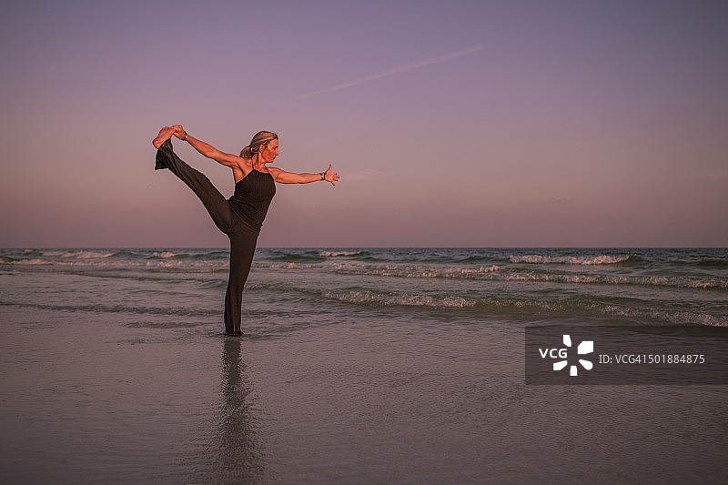成熟的女人练习瑜伽姿势在海滩上日落图片素材