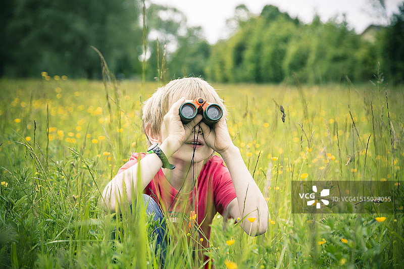 小男孩坐在草地上用望远镜看东西图片素材