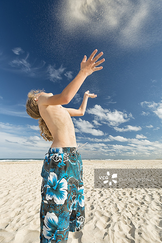 澳大利亚，新南威尔士州，波茨维尔，沙滩上的男孩向空中扔沙子图片素材