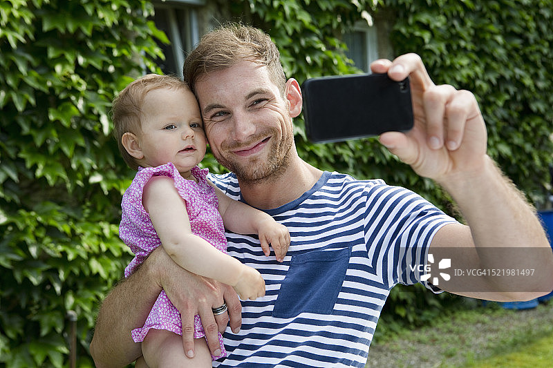 中年成年男子带着女儿在花园里用智能手机自拍图片素材