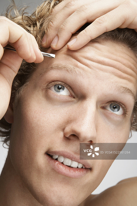 男人在用镊子拔前额上的头发图片素材