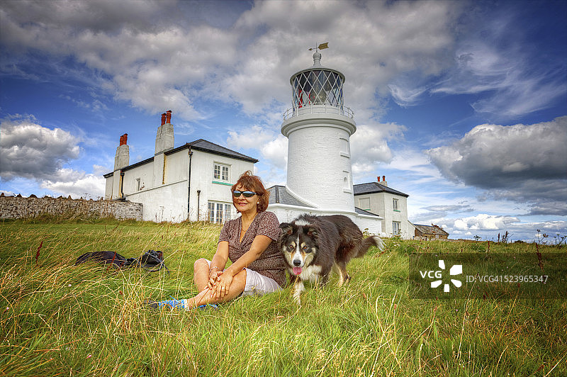 成熟微笑的西班牙老人和狗坐在草地岬角图片素材