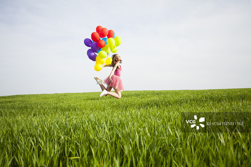 快乐的年轻女子拿着气球在球场上跳跃图片素材