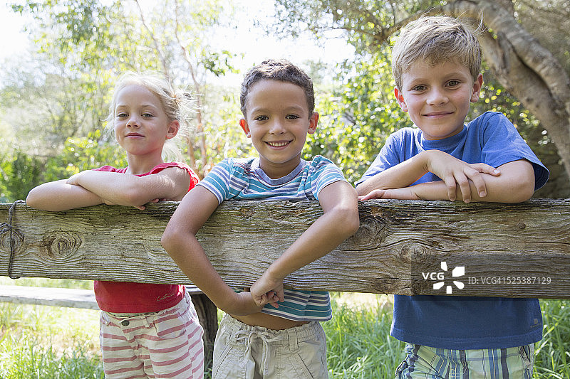 三个孩子倚在花园的篱笆上图片素材