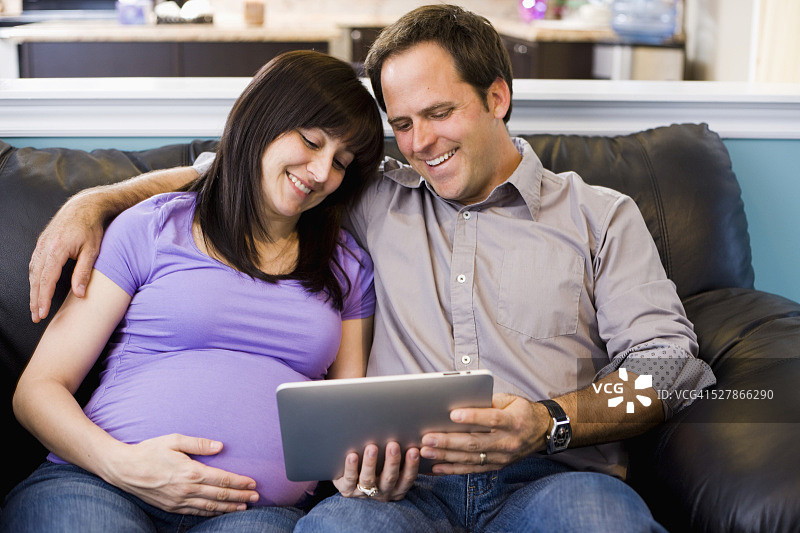 孕妇和丈夫坐在沙发上看平板电脑图片素材