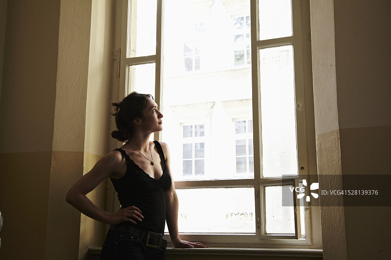一个年轻女子站在楼梯上望着窗外图片素材