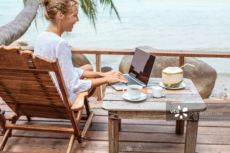 年轻女子用笔记本电脑工作喝着咖啡，吃着小椰子图片素材