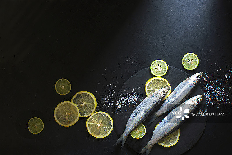 冰鲜生沙丁鱼与香草和柠檬片在黑色的背景。图片素材