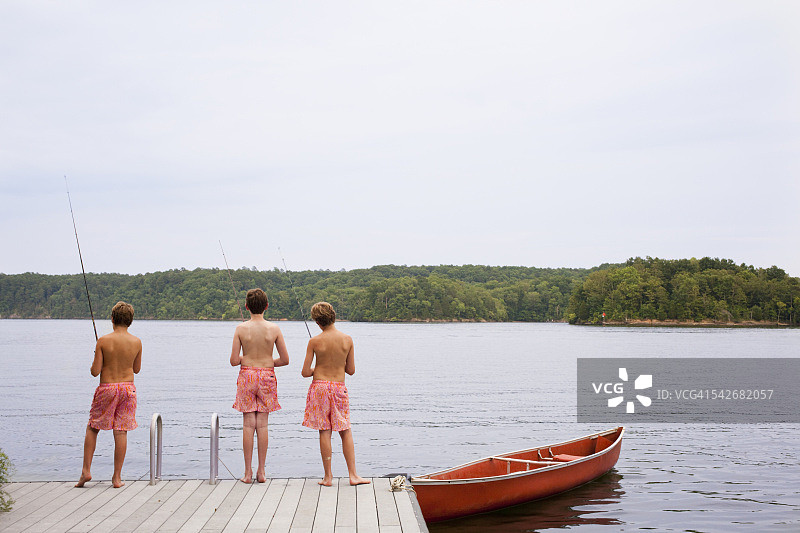 穿着短裤的小男孩们在独木舟旁边的码头钓鱼图片素材