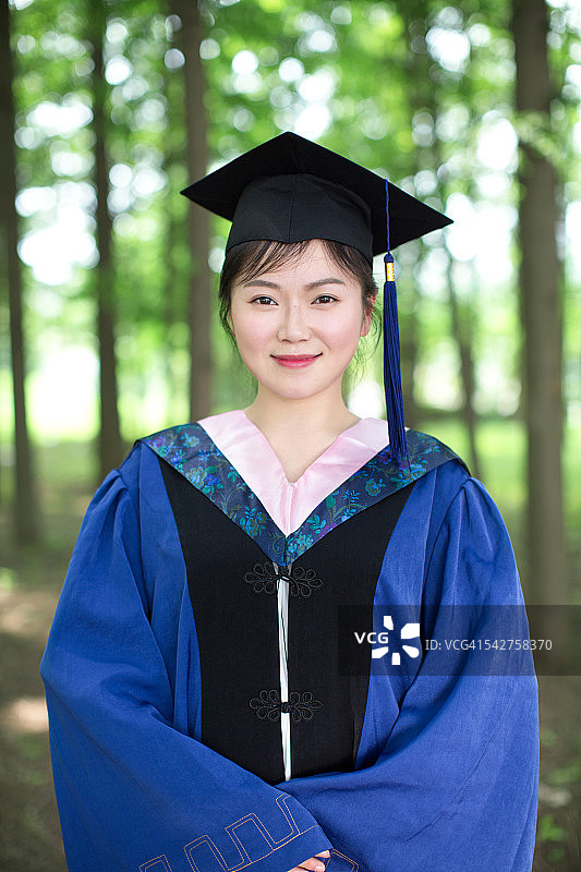 年轻的亚洲女性毕业生在帽子和长袍，微笑和看着镜头图片素材