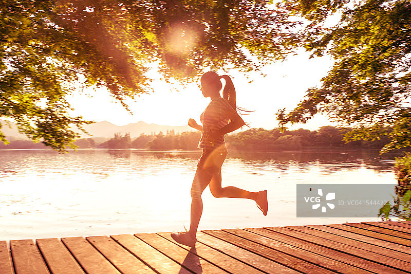 日落时分，年轻的亚洲女子在湖边的码头上奔跑图片素材