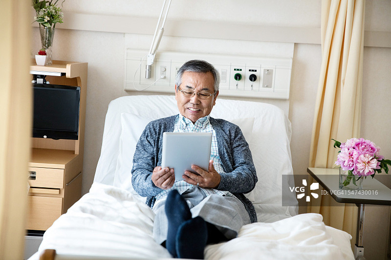 老人在医院病床上使用平板电脑图片素材