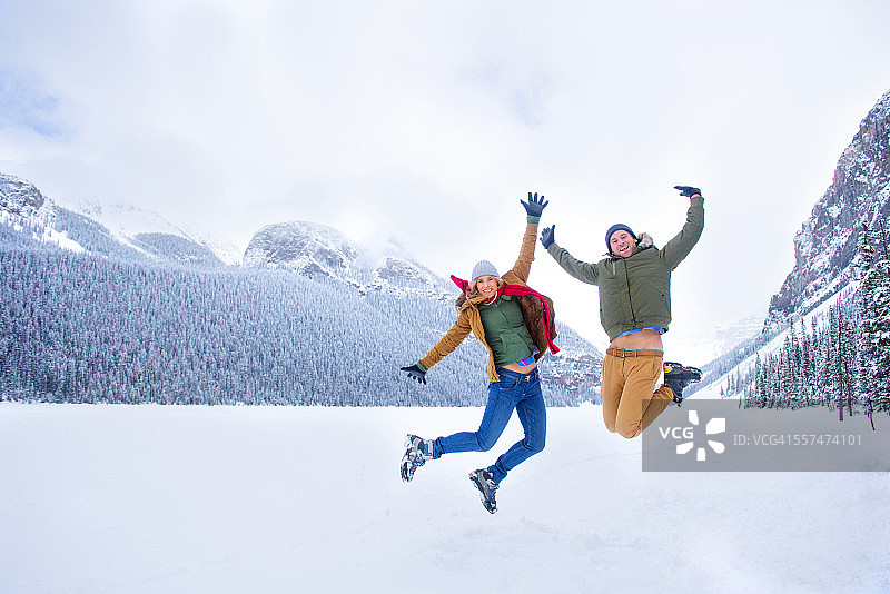 一对白人夫妇在加拿大阿尔伯塔省路易丝湖附近的雪山欢快地跳跃图片素材