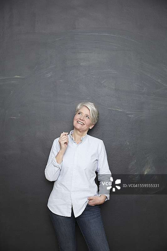 微笑的成熟的老师站在黑板上仰视图片素材