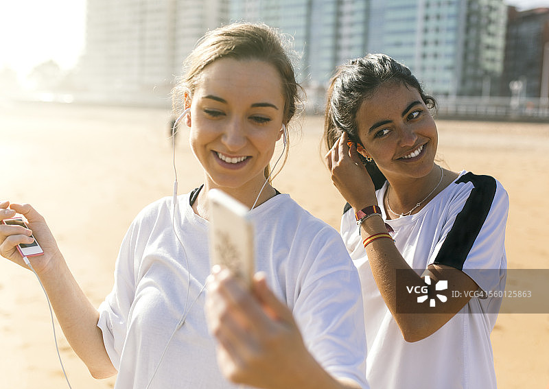 西班牙，希洪，海滩上两个戴着耳机的活泼的年轻女人图片素材