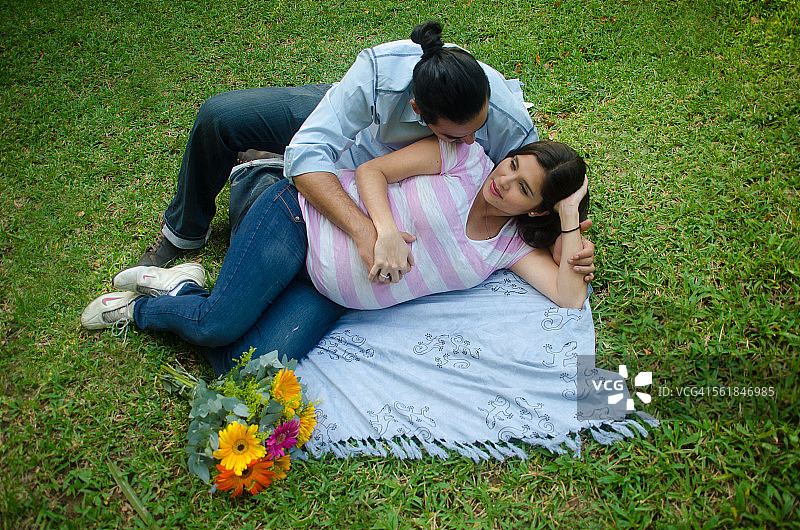 一对年轻的怀孕夫妇躺在草地上的毯子上图片素材