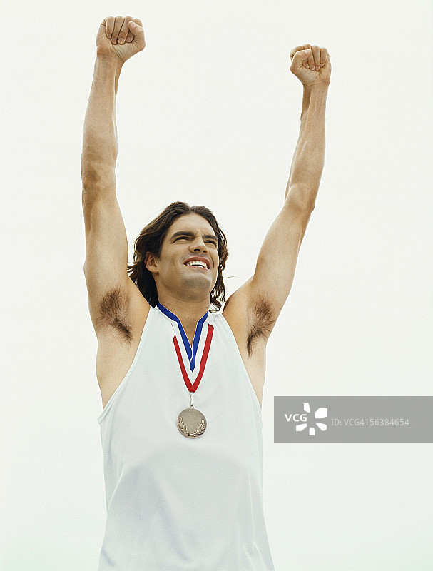 低角度的一个男运动员戴着一枚奖章，他的手举起图片素材