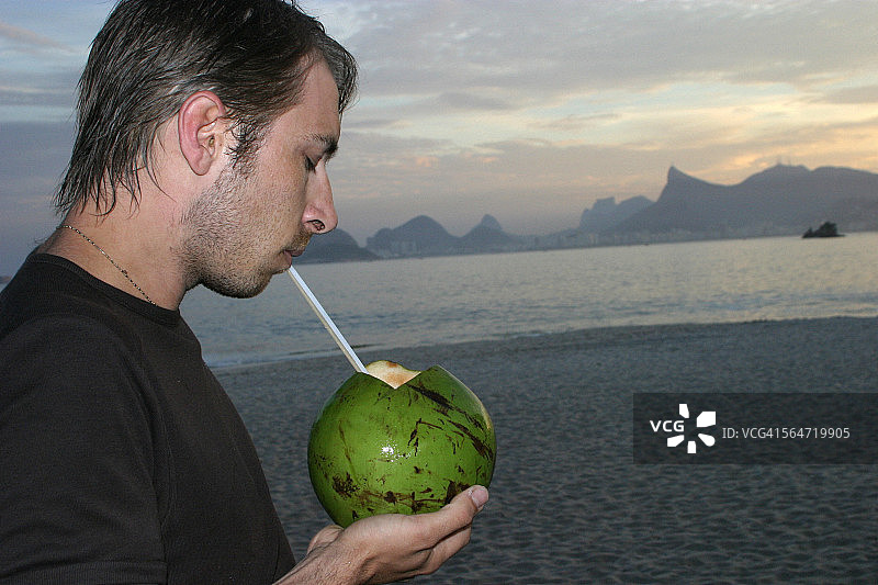 海滩上的男人用椰子喝图片素材