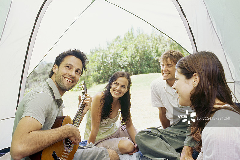 一个年轻人和他的朋友坐在帐篷里弹吉他图片素材