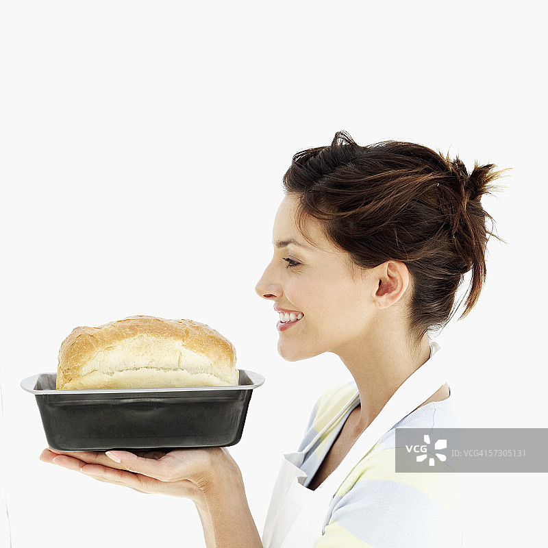 一个年轻女子的侧影，手里拿着刚烤好的面包图片素材