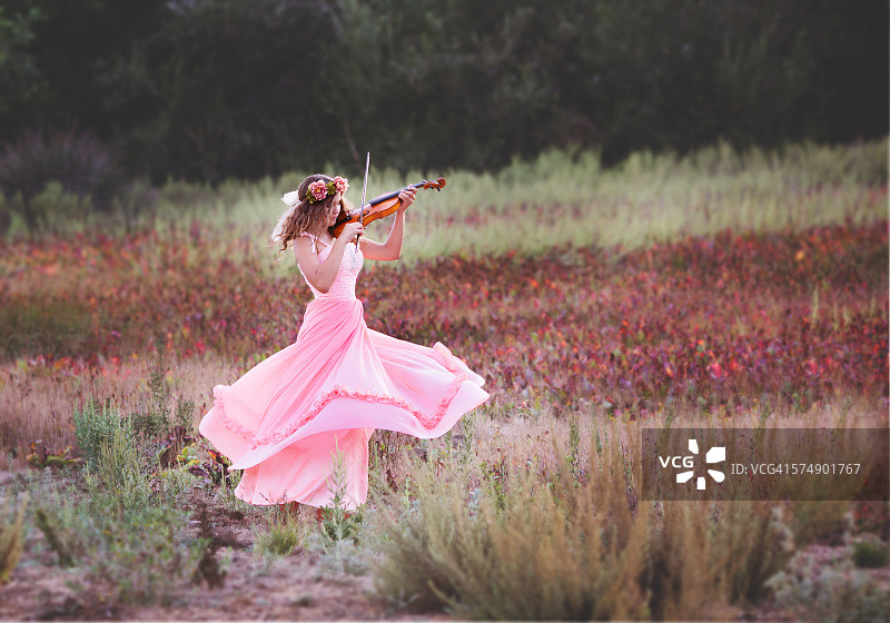 女孩一边拉小提琴一边在田野里跳舞图片素材