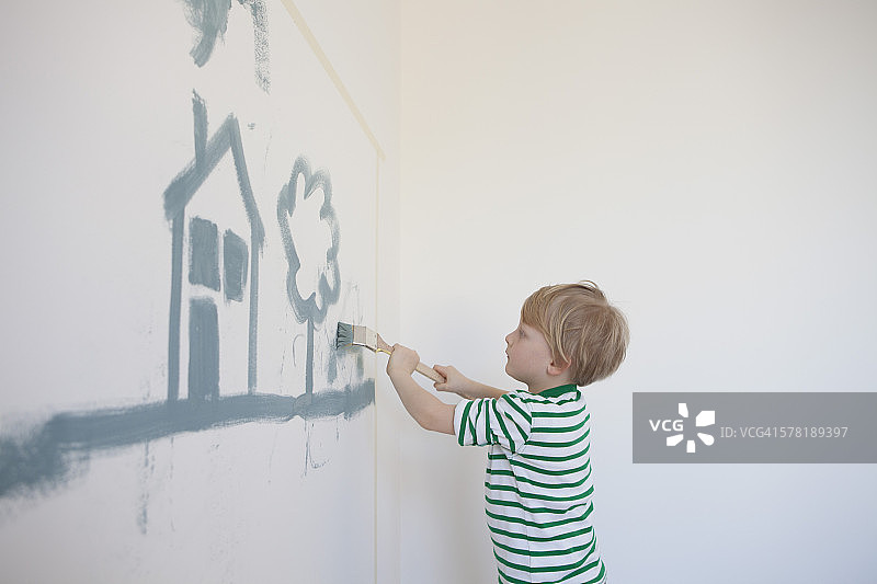 小男孩在他新房间的墙上画房子和树图片素材