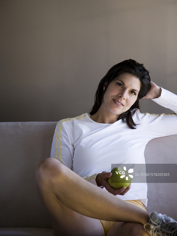 拿着青苹果坐在沙发上的女人图片素材