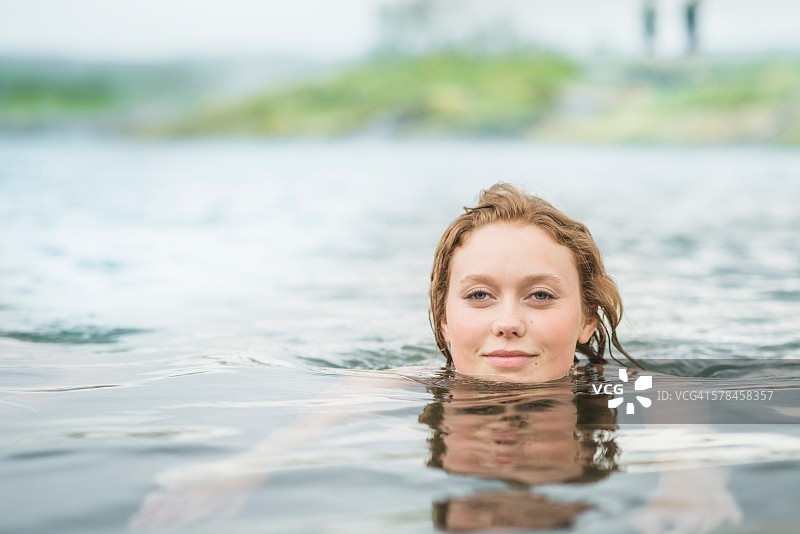 宁静的年轻女子在秘密泻湖温泉游泳的肖像(Gamla Laugin)， Fludir，冰岛图片素材