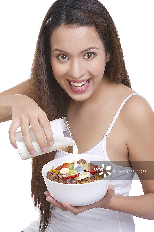 一个女人往一碗麦片里倒牛奶的肖像图片素材