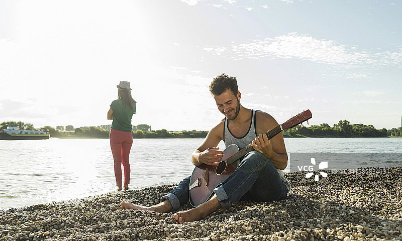 一个年轻人在河边和一个女人弹吉他图片素材