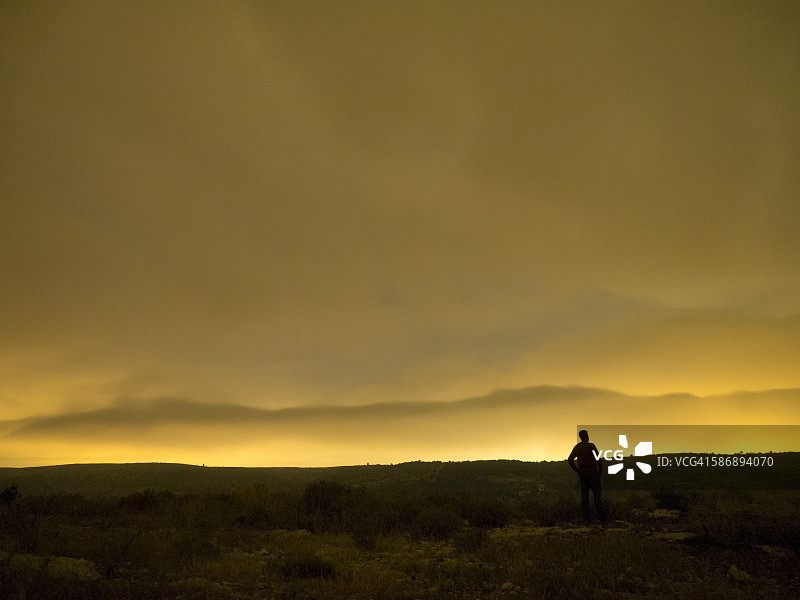 一个人的剪影，以交叉光在山顶的一个夜晚的云橙色颜色图片素材