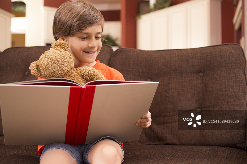 孩子在家里和泰迪熊一起看书。图片素材