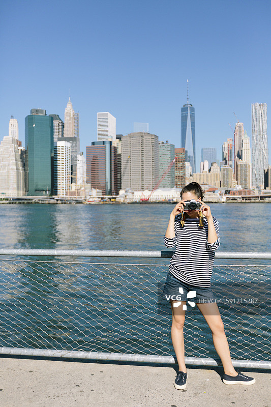 美国，纽约市，年轻女子在天际线前用相机拍照图片素材