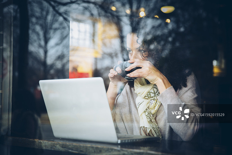 混血女人喝咖啡和使用笔记本电脑在咖啡馆图片素材