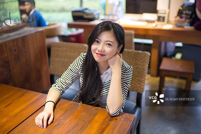 年轻的亚洲女人微笑的肖像在桌子旁图片素材