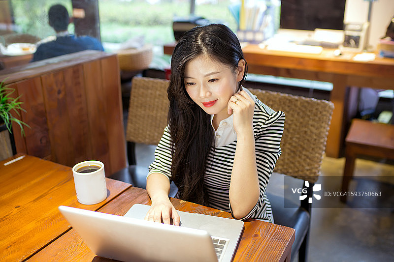 一个年轻的亚洲女人在咖啡馆用笔记本电脑图片素材