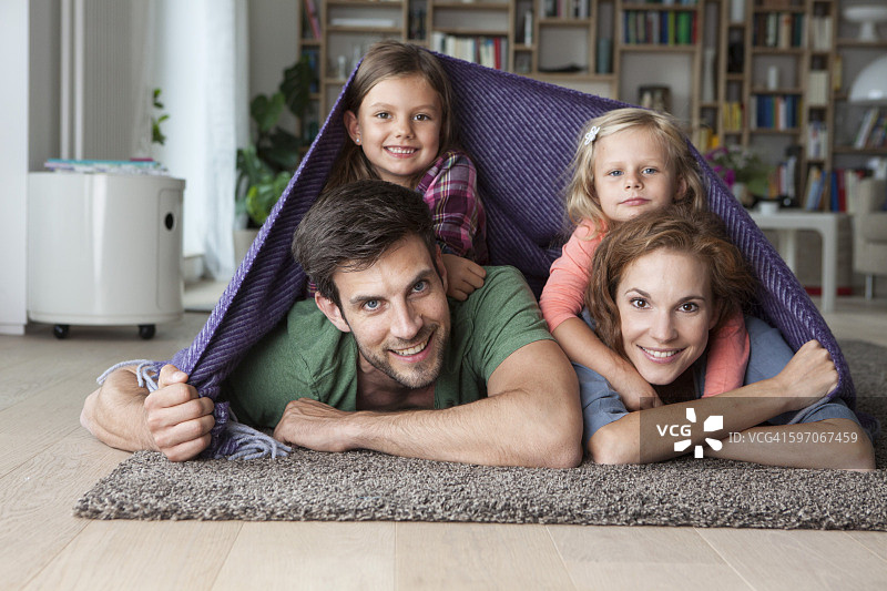 一对夫妇和她的小女儿一起躺在客厅的地板上，上面盖着毯子图片素材