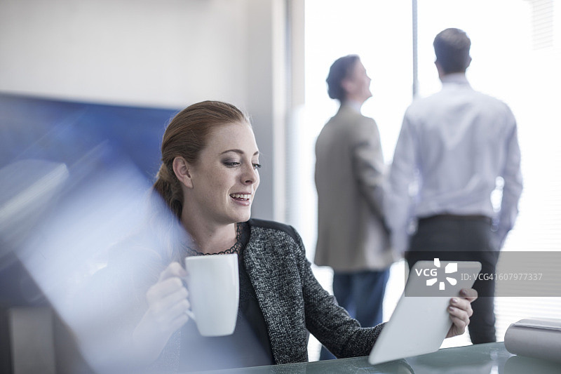 微笑的女人在办公室拿着一杯咖啡和数字平板电脑图片素材