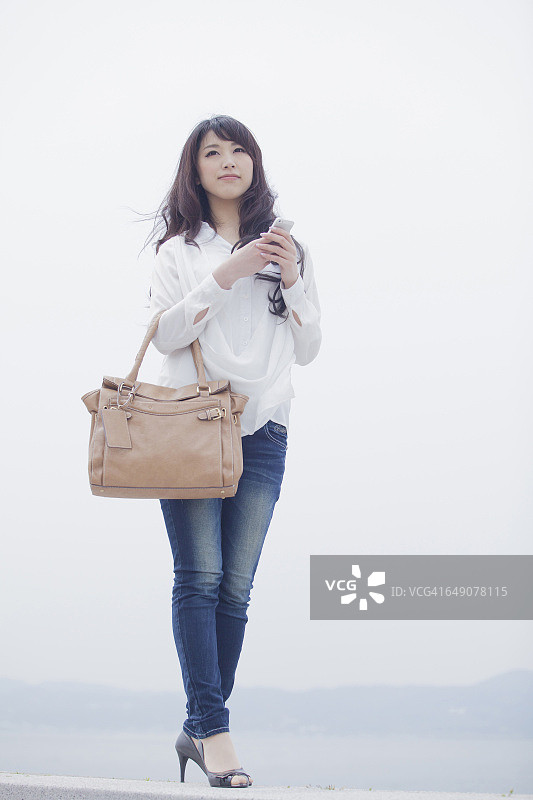 拎着包拿着智能手机的日本女人图片素材